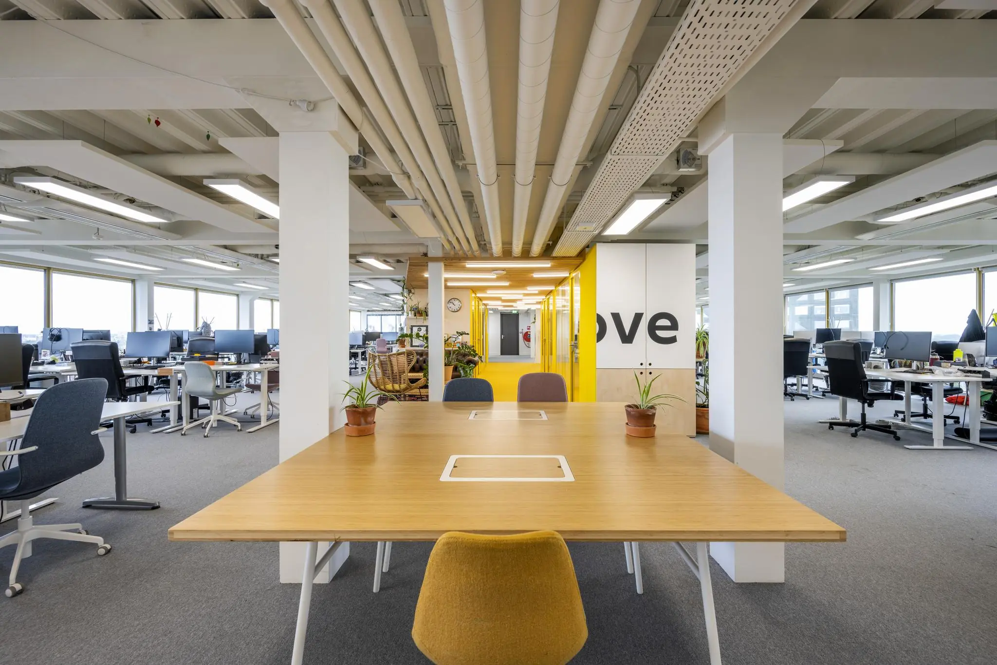 Moderne open kantoorruimte aan de James Wattstraat met werkplekken, vergadertafel en opvallende gele accenten.